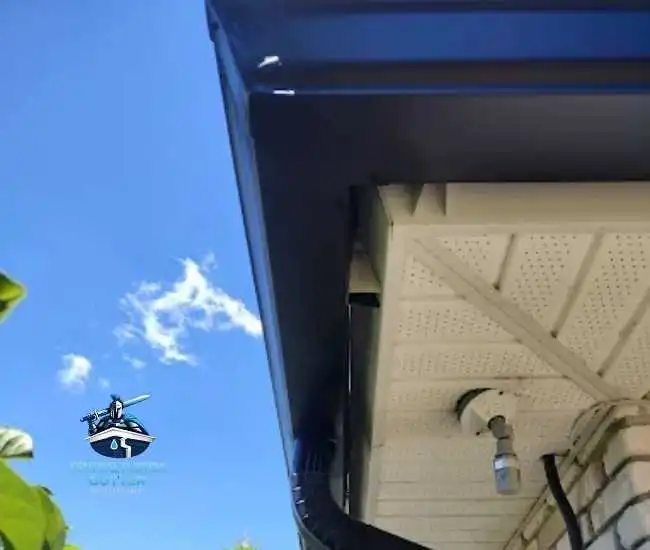 "Black seamless gutter corner and downspout installed with white vented soffit and a security camera."