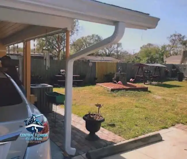 "White seamless aluminum gutter and downspout installed on a residential porch overlooking a backyard."