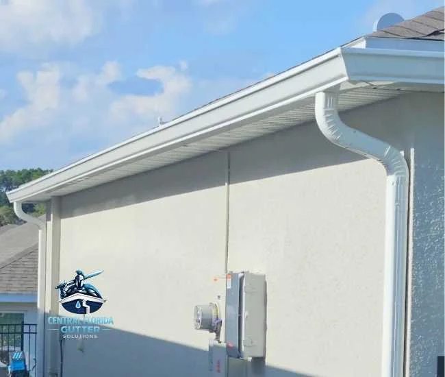 "White seamless aluminum gutter and downspout installed on a stucco home under a clear blue sky."