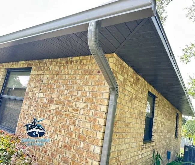 "Grey seamless aluminum gutter and downspout installed on a brick home with dark grey soffits."