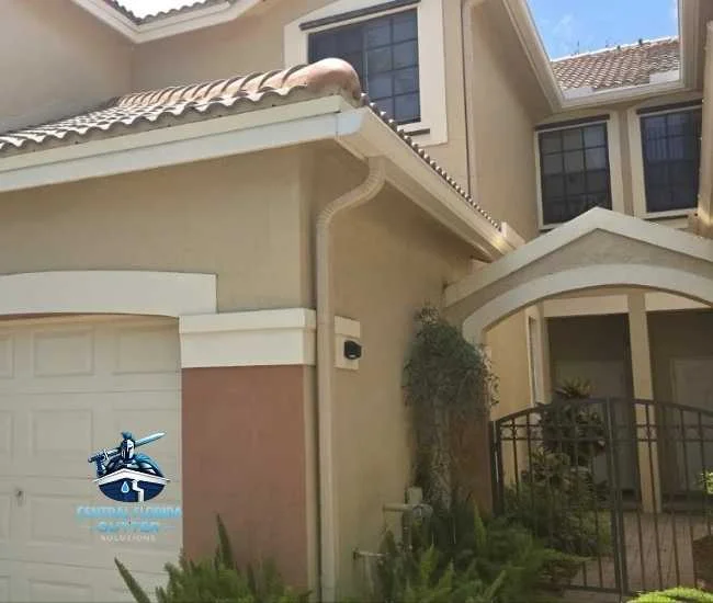A multi-story tan home with a terracotta tile roof, featuring newly installed cream-colored gutters and a downspout along the entryway.