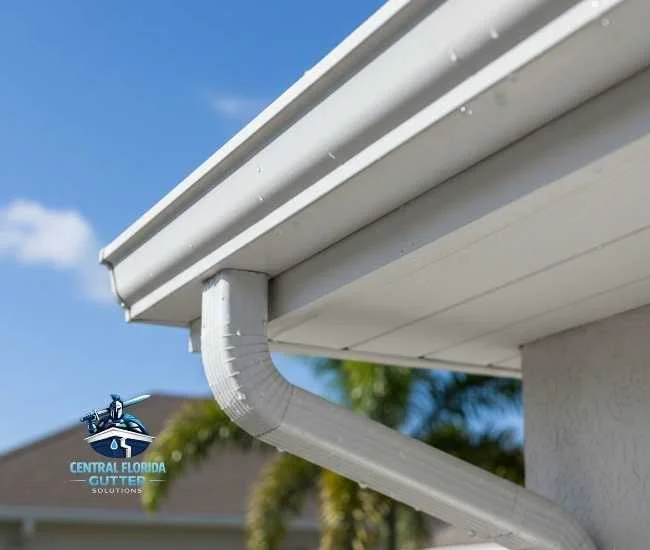 Close-up of a white gutter and a curved downspout attached to a light gray house with a matching white soffit.