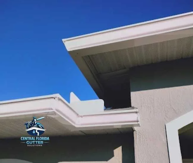 Low-angle shot of clean white gutters and matching soffit installed on a light gray house under a clear blue sky.