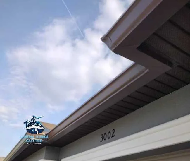 Upward view of dark gutters and tan perforated soffit panels installed on a home under a clear blue sky.