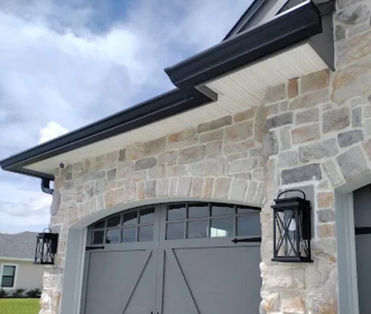 Close-up of a modern home exterior featuring a stone veneer facade, grey garage doors, and black seamless gutters.